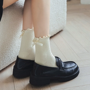 Mid-calf white ruffle socks with bows paired with platform loafers in a soft home setting