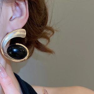 Close-up of elegant gold metal stud earring with a large black oval resin stone on model ear