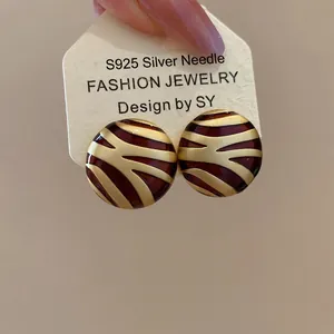 Detailed close-up of geometric round enamel earrings with brown and gold zebra pattern
