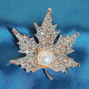 Detail of rose gold maple leaf brooch with white crystals and a large white pearl