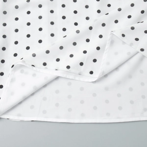 Close-up of white polka dot fabric showing ruffled edge stitching and inner lining detail