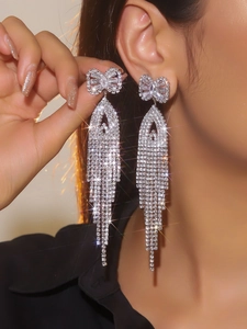 Macro detail of luxury silver bow earrings with long sparkling tassel chain and zircon