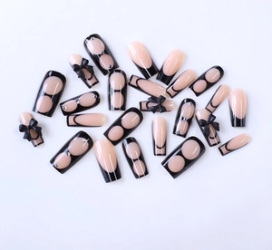Close-up of black French press-on nails with 3D bows and rhinestones on white base