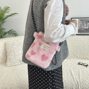 Detailed shot of pink plush crossbody bag with red hearts and woven shoulder strap