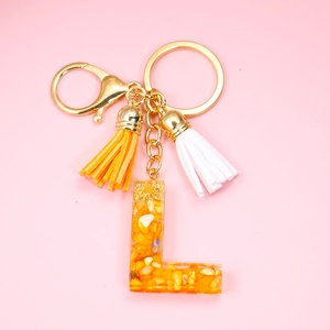 Close-up of resin letter L keychain with yellow stones and gold fringe tassels