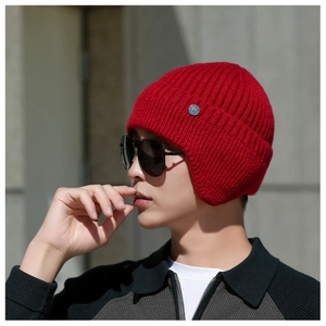 Detail of red cable knit winter hat with earflaps and small silver metal logo button