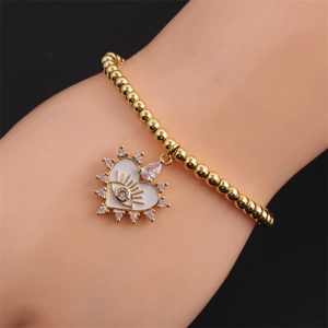 Close-up of gold beaded elastic bracelet featuring a white enamel evil eye heart charm