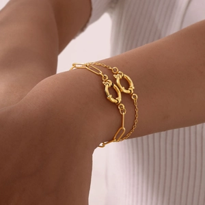 Detail of a gold double-layer bracelet with paperclip chain and circle links on a wrist