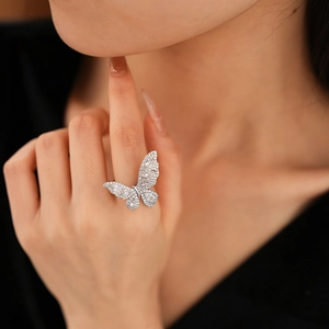 Detail of a sparkling zircon butterfly ring featuring a polished silver finish on model's finger