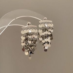 Detailed close-up of silver sequin tassel earrings on a display stand showing metallic luster