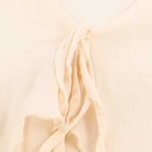 Detalle del escote en V y cordón con volantes en el vestido midi de gasa crema