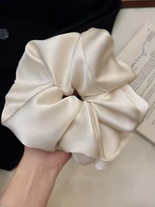 Macro detail of oversized champagne satin scrunchie with glossy silk-like texture