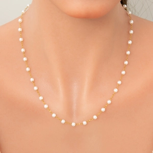 Detailed close-up of a refined pearl necklace with gold chain on model neck