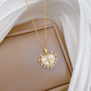 Detail der goldenen Herz-Kette mit Kreuz und Perlen auf elegantem Seidenstoff