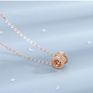 Macro shot of rose gold hexagonal pendant with sparkling stones on light blue background