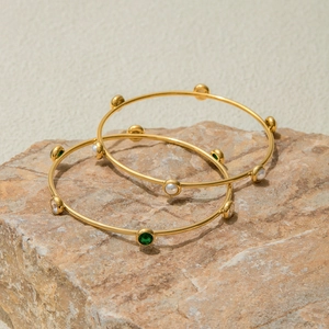Bracciali in acciaio inossidabile dorato 18k con gemme verdi e perle su una pietra naturale