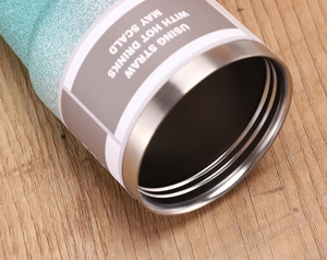 Detail of glitter turquoise tumbler rim and warning label on natural wood surface