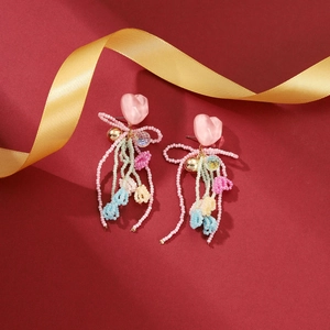 Close-up of pink heart earrings with colorful beaded tassels and festive silk ribbon