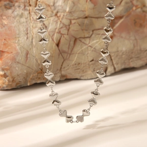Macro shot of silver textured heart-link chain necklace displayed on a natural rock