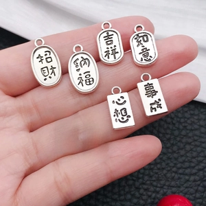 Detail of hand holding zinc alloy lucky charms with engraved Chinese blessings for DIY crafts