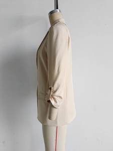 Detail of beige blazer sleeve with unique buttoned pleated cuff on a mannequin