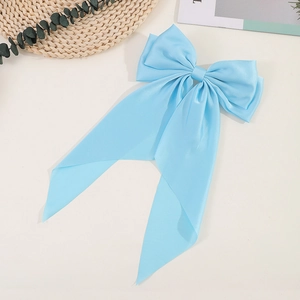 Detail of a large blue satin bow hair clip with elegant ribbons on a neutral background