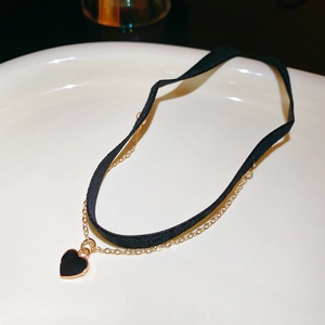 Detail of a double-layer black velvet choker with a gold heart pendant on white porcelain