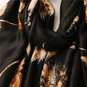 Close-up of black cotton-linen scarf featuring gold foil feather patterns and woven texture