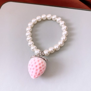 Close-up of pearl bracelet with pink flocked strawberry pendant and zircon detail