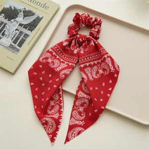Macro detail of red paisley bandana hair scrunchie with long ribbons in a beige tray