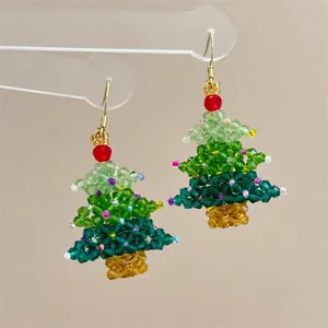 Macro shot of handmade beaded Christmas tree earrings with green crystals and red accents