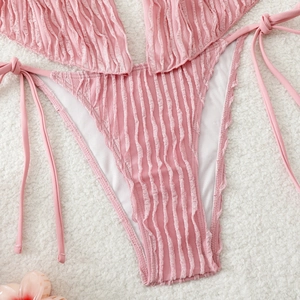 Detailed view of pink bikini bottom with ruffled texture and side tie strings on soft rug