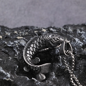 Artistic shot of a vintage silver koi fish pendant on a black stone with a pearl chain