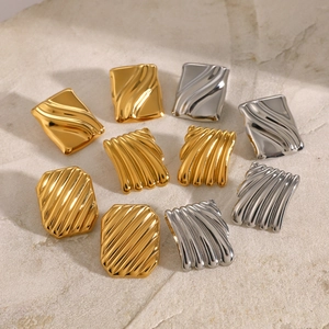 Detailed view of textured irregular gold and silver square earrings on stone surface