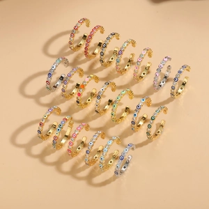 Anelli malocchio in oro e argento con zirconi colorati su sfondo beige neutro