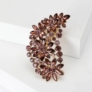 Detailed shot of golden floral brooch with deep purple crystals on a white platform
