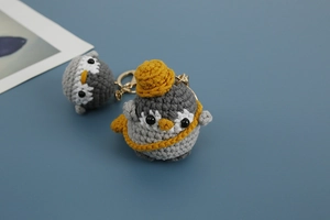 Close-up of handmade crochet penguin with yellow hat and metallic lobster clasp detail