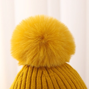 Primer plano de un gorro de punto amarillo con un gran pompón de piel sintética suave