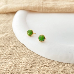 Close-up of green natural stone earrings with 18K gold-plated brass frames on a ceramic tray
