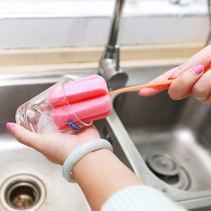 Pink kitchen sponge cleaning brush with long handle used for washing a glass cup