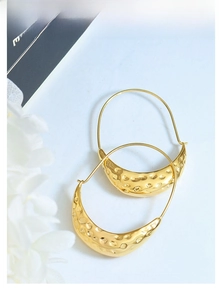 Close-up of golden boat-shaped earrings featuring textured hammered metal finish