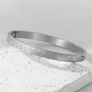 Macro shot of silver stainless steel bangle with detailed engraved wave patterns