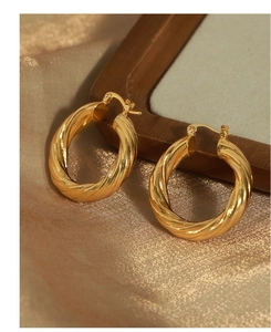 Macro shot of gold twisted hoop earrings resting on elegant silk and wooden frame