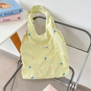 Detail of embroidered colorful bows on a cream seersucker tote bag with brand label