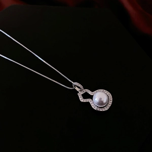 Close-up of silver gourd earring with pearl and zircon inlay against a dark background
