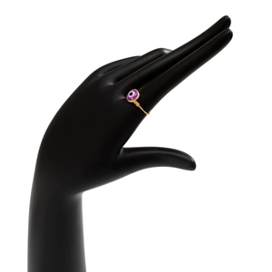 Close-up of golden wire-wrapped ring with purple evil eye bead on a black hand display