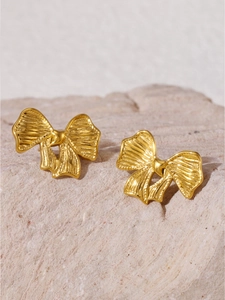 Gros plan de boucles d'oreilles nœud dorées avec texture brossée sur fond de pierre naturelle