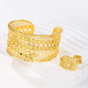 Detail view of gold hollow cuff bracelet and ring set with intricate ethnic leaf pattern