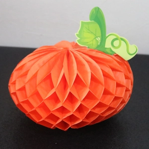 Detailed view of an orange pumpkin honeycomb paper decoration with green leaf for fall parties