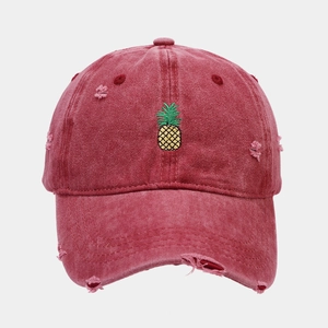 Detailed view of yellow pineapple embroidery on vintage distressed red denim baseball cap
